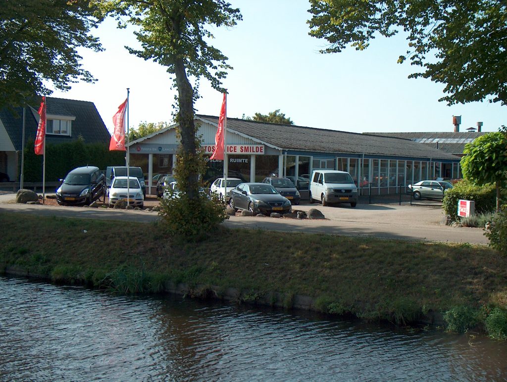Het pand van Autoservice Smilde met vlaggen, aan het water in Smilde