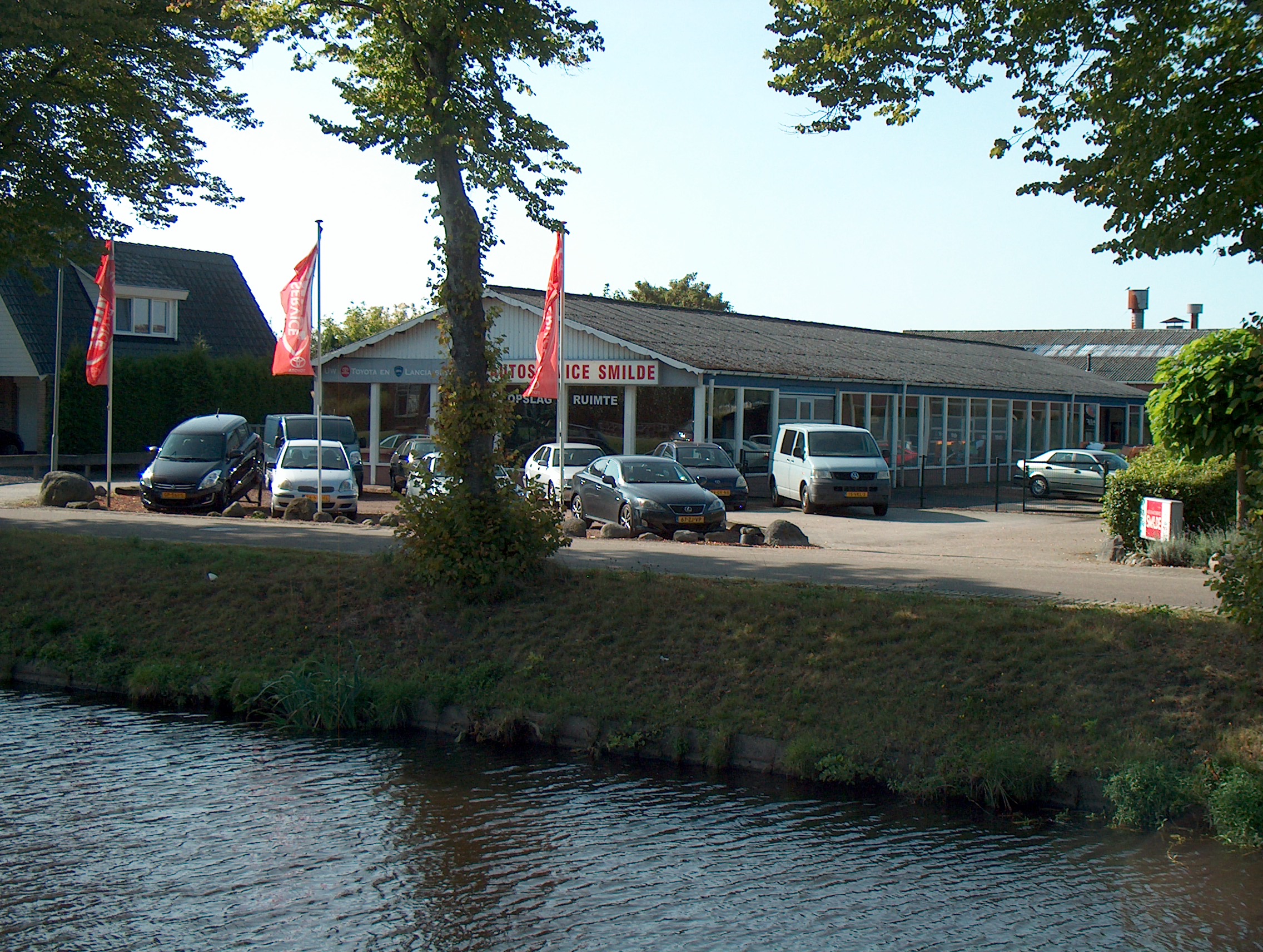 Het pand van Autoservice Smilde met vlaggen, aan het water in Smilde